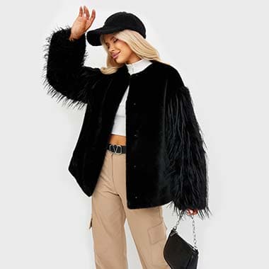Девушка в черной шубе стоит и касается кепки